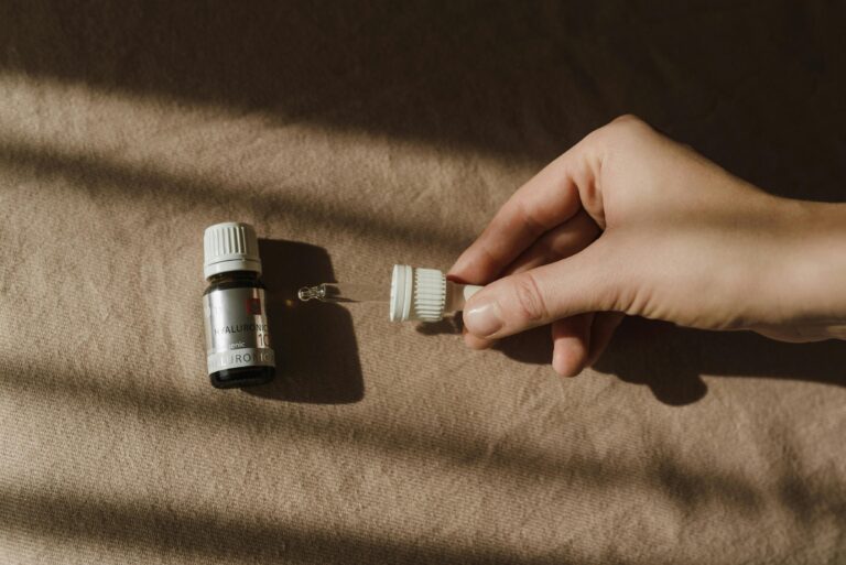 Close-up of a hand holding a dropper next to a skincare bottle on a textured surface.