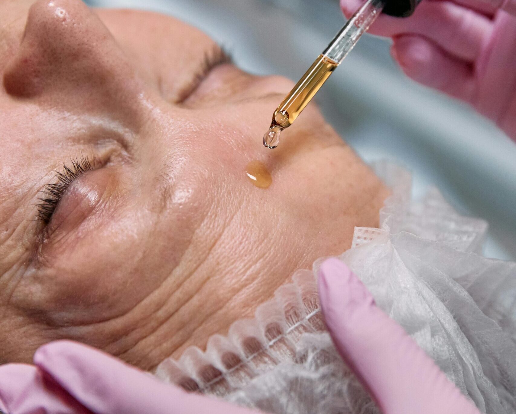 Senior woman receiving a facial serum treatment in a spa setting.